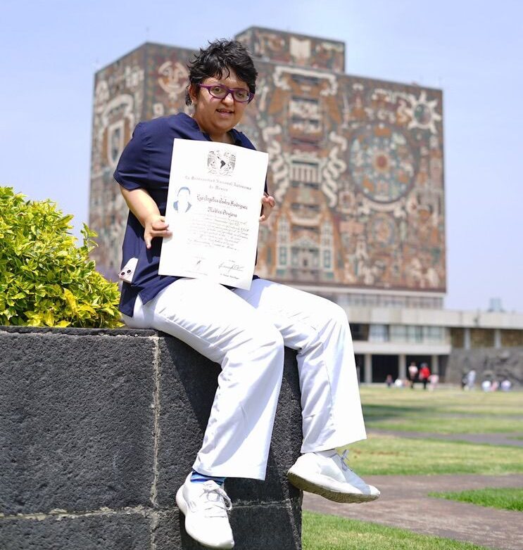 mujer con su título en mano en el exterior de la UNAM